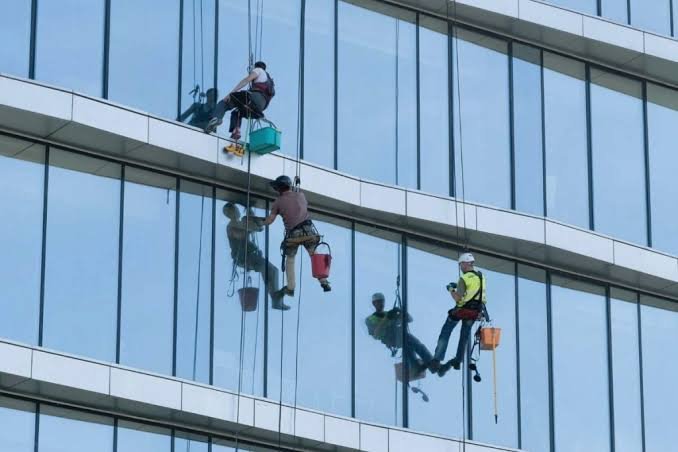 Alpiniści myjący szklaną fasadę metodą tradycyjną na linach